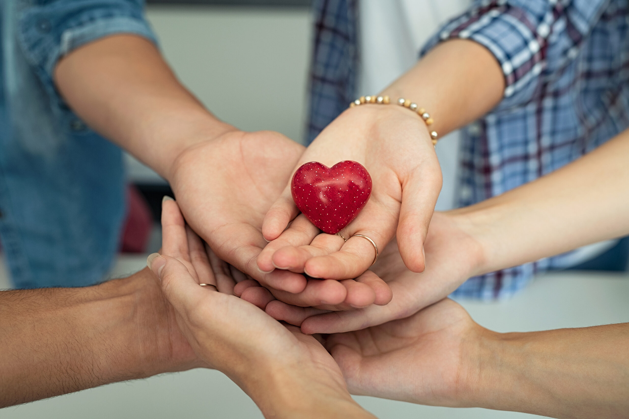 Close up of friends hands holding a red heart shape. Top view of